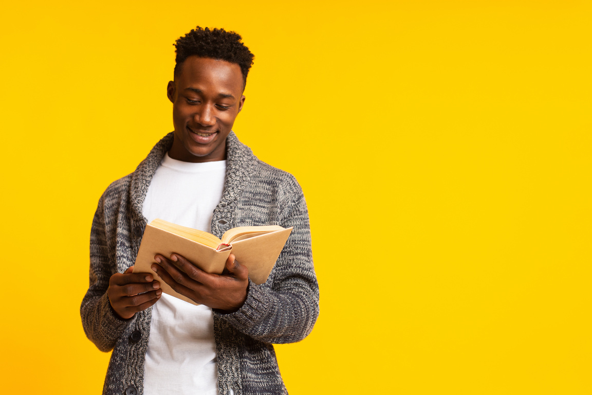 Romantic african guy reading poetry in old book on yellow